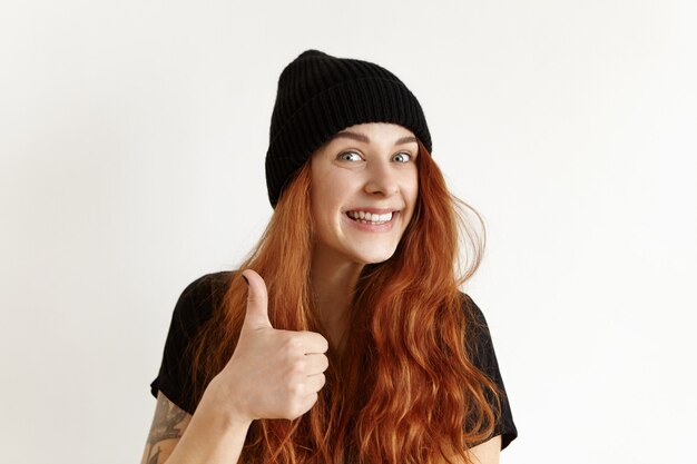 Feliz alegre garota europeia com tatuagem e penteado bagunçado, mostrando o polegar para cima