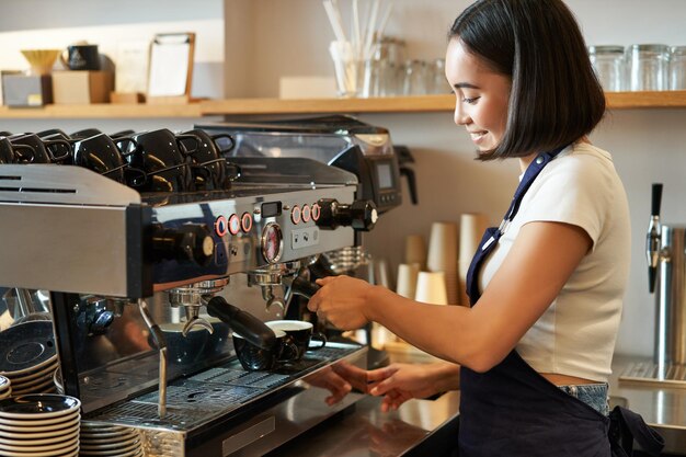 Foto grátis feliz barman sorridente barista usando a máquina de café para preparar o pedido fazendo cappuccino ou latte vestindo