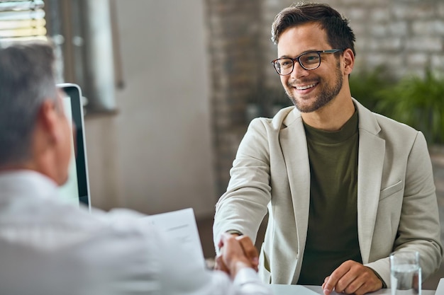 Feliz candidato do sexo masculino aperto de mão com um gerente após uma entrevista de emprego bem-sucedida no escritório