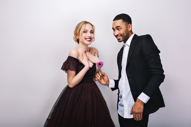 Feliz casal apaixonado, comemorando o dia dos namorados. mulher jovem e atraente loira com vestido de luxo, homem bonito de smoking, dando flores, sorrindo, emoções positivas.