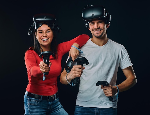 Feliz casal de jogadores com controladores e fones de ouvido VR. Isolado em fundo escuro.