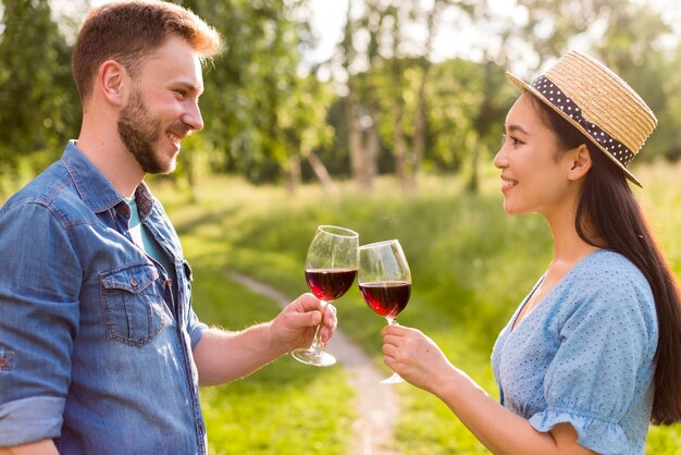 Feliz casal multiétnico tinindo copos de vinho no parque