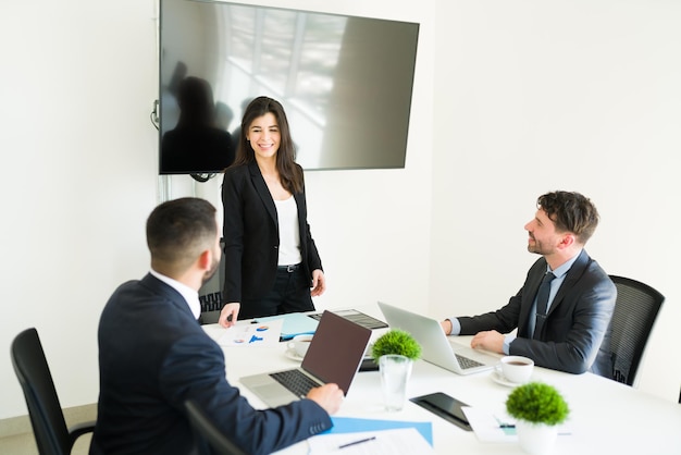 Feliz chefe feminina de terno sorrindo e dando boas notícias para seus colegas de trabalho durante uma reunião de trabalho