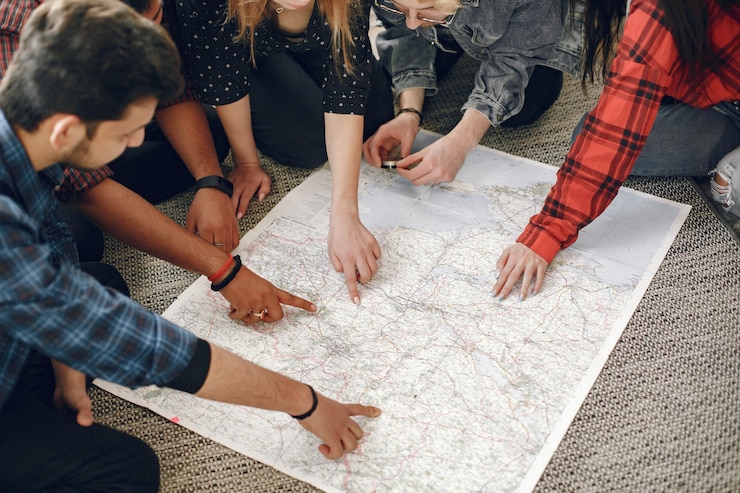 Foto grátis feliz círculo de amigos planejando uma viagem. trotadores do globo inspecionando um mapa em casa. etnia europeia e indiana.