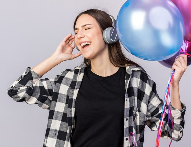 Feliz com os olhos fechados, uma jovem linda usando fones de ouvido segurando balões