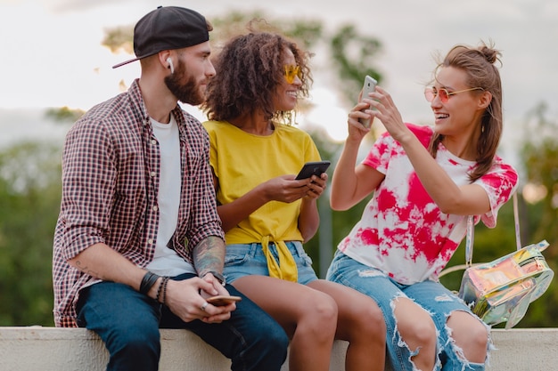 Feliz companhia jovem e elegante de amigos sentados no parque, homens e mulheres se divertindo juntos