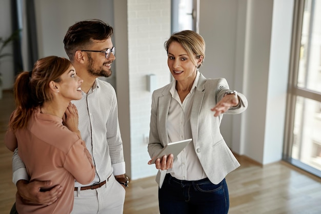 Feliz corretor de imóveis conversando com um casal enquanto mostra um novo apartamento