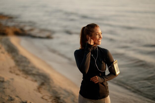 Feliz desportista se preparando para o treino matinal e ouvindo música no fone de ouvido enquanto está na praia Copiar espaço