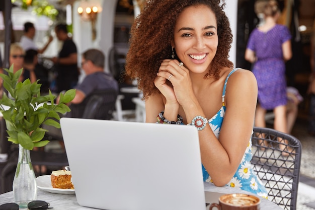 Feliz e bem-sucedida jovem e talentosa redatora afro-americana trabalhando em um laptop em um restaurante