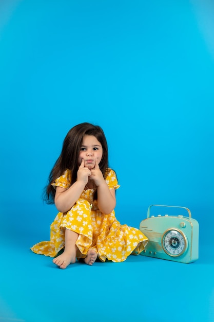 Feliz e fofa garotinha roupas de bebê amarelo na moda posando estúdio em fundo azul