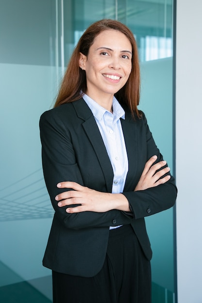 Feliz empresária bem-sucedida, ruiva, vestindo terno formal, de pé com os braços cruzados e sorrindo