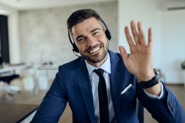 Feliz empresário acenando enquanto trabalhava no escritório e olhando para a câmera