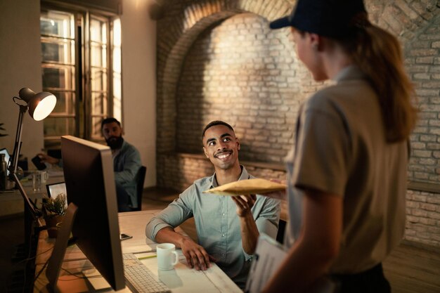 Feliz empresário afro-americano recebendo pacote do entregador enquanto trabalhava em sua mesa no escritório