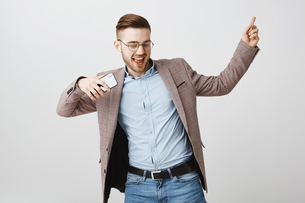 Feliz empresário dançando alegre com smartphone, ouvindo música em fones de ouvido sem fio