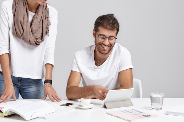 Feliz empresário e sua assistente no escritório perto da mesa, trabalham com documentos, bebem café e usam aparelhos eletrônicos