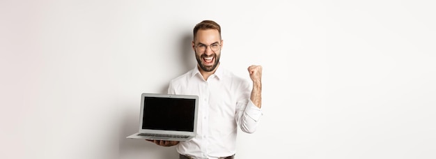 Foto grátis feliz empresário mostrando a tela do laptop fazendo punho e regozijando-se com a conquista online