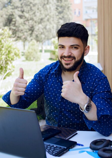 Feliz empresário segurando os polegares enquanto olha para a câmera enquanto trabalha