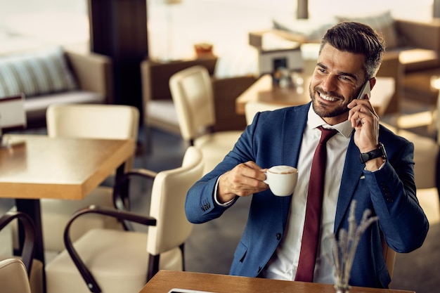 Feliz empresário tomando café e falando ao telefone em um café