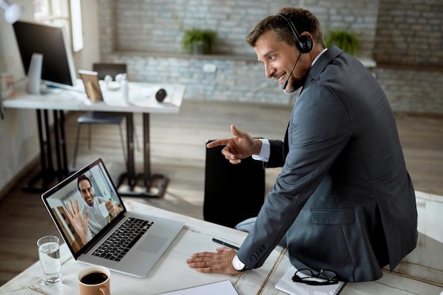 Feliz empresário usando laptop enquanto tem reunião online com seu colega de trabalho no escritório