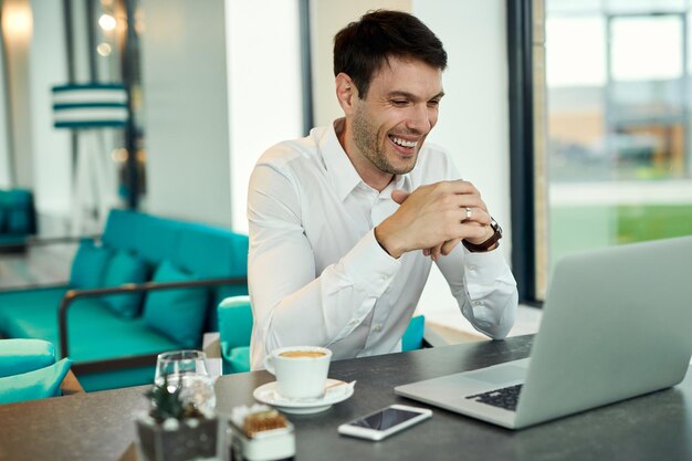 Feliz empresário usando laptop enquanto toma café em um café