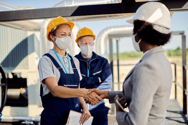 Foto grátis feliz engenheiro civil e empreiteiro usando máscaras protetoras enquanto aperta as mãos no canteiro de obras