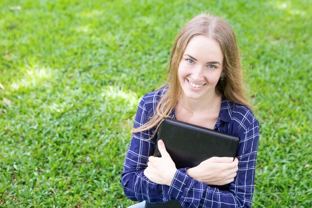 Feliz estudante moderno com laptop sentado no parque