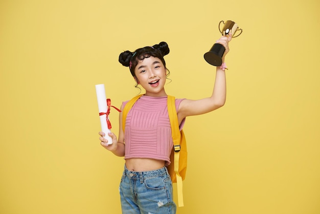 Foto grátis feliz graduada asiática com um diploma e troféu mostra um gesto de vitória e sucesso