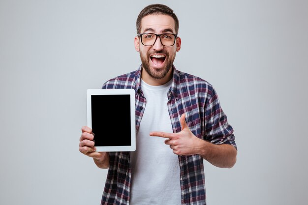 Feliz homem barbudo em óculos mostrando a tela do computador tablet em branco