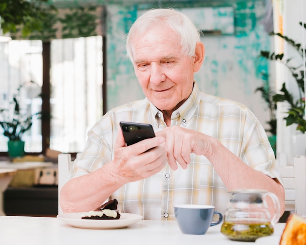 Feliz homem idoso sentado no café e mensagens de texto no celular