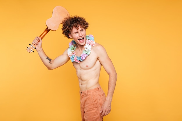 Feliz homem sem camisa animado segurando o ukulele e olhando para longe