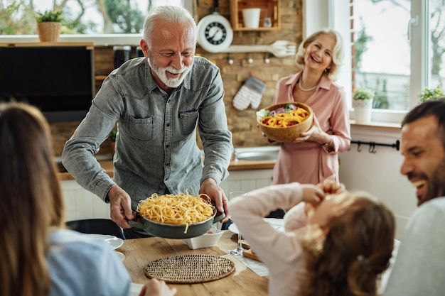 Feliz homem sênior servindo comida na mesa de jantar enquanto almoça em família em casa