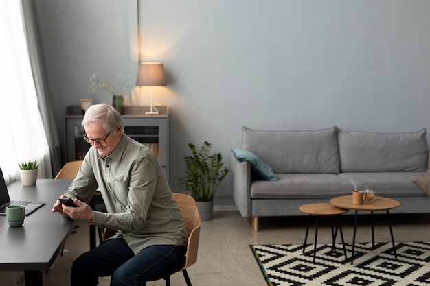 Feliz homem sênior usando smartphone na sala de um apartamento moderno