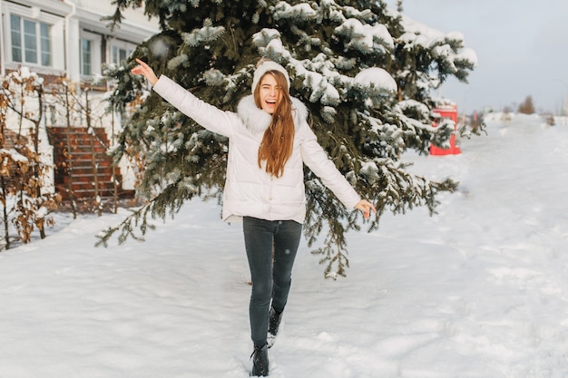 Feliz inverno congelado na manhã ensolarada na rua de uma mulher bonita alegre se divertindo na neve.