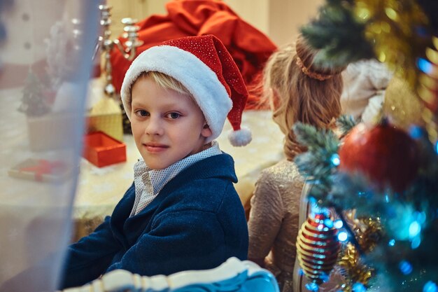 Feliz irmã e irmão sentados à mesa em uma elegante sala de estar decorada para o Natal.