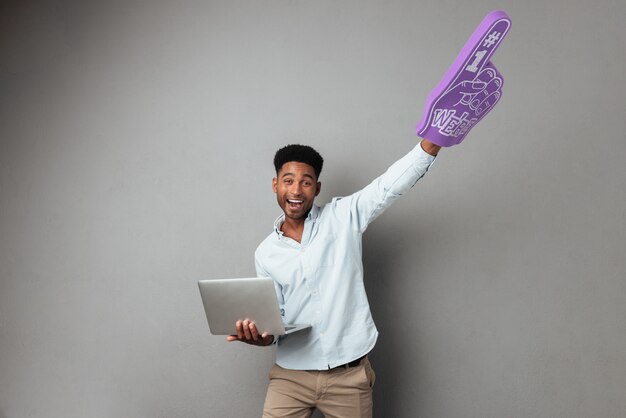 Feliz jovem Africano segurando computador portátil e dedo de espuma