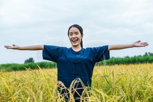 Feliz jovem agricultora asiática em pé e de braços abertos em um campo de arroz orgânico