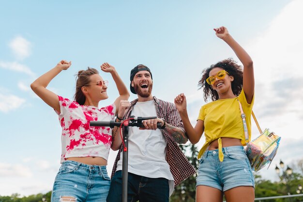 Feliz jovem companhia de amigos sorridentes dançando andando na rua com scooter elétrico, homens e mulheres se divertindo juntos