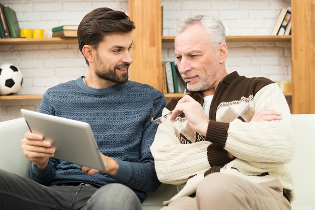 Feliz jovem e envelhecido homem usando tablet no canapé