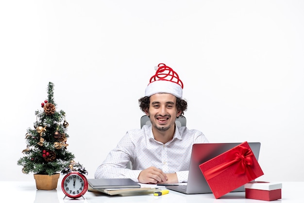 Feliz jovem empresário positivo com chapéu de papai noel engraçado, comemorando o natal no escritório em fundo branco