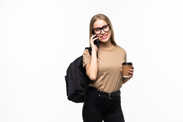 Feliz jovem estudante universitária com mochila e livros falando no celular, isolado na superfície branca