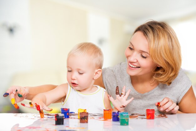 Feliz jovem mãe com uma pintura de bebê pelas mãos em casa.