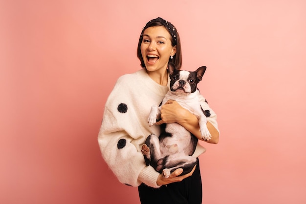 Foto grátis feliz jovem morena caucasiana segurando cachorro preto e branco nos braços no fundo rosa, mostrando o conceito de carinho