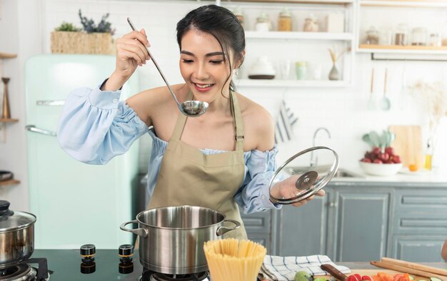 Feliz linda jovem asiática cozinhando sopa e cheirando sopa na cozinha