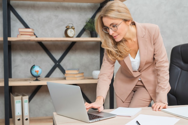 Feliz loira jovem empresária digitando no laptop no local de trabalho no escritório