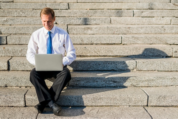 Feliz, maduras, homem negócios, sentando escadaria, usando computador portátil, em, ao ar livre