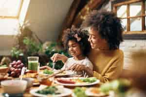 Foto grátis feliz mãe afro-americana e filha comendo na mesa de jantar