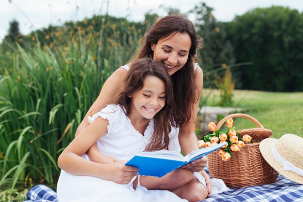 Feliz mãe e filha lendo livro no piquenique