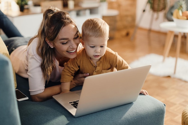 Feliz mãe solteira e seu filho pequeno usando laptop na sala de estar