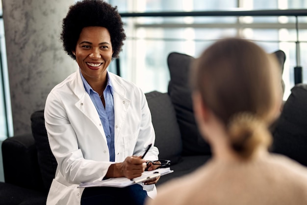 Feliz médico afro-americano falando com paciente do sexo feminino durante uma sessão de psicoterapia