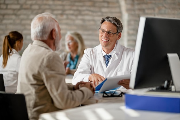 Foto grátis feliz médico masculino explicando o prontuário médico para seu paciente sênior durante a reunião de aconselhamento na clínica
